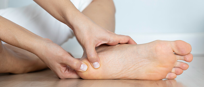 A Foot on the Floor Showing the Bare Sole, Hands Feeling the Heel