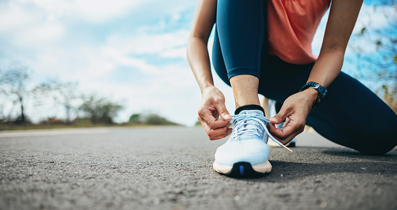 Woman Tying Shoe on Pavement