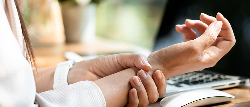 Woman Grasping Her Wrist in Front of a Computer