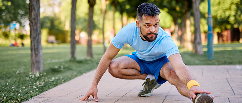 Older Man Crouching and Stretching Legs in a Park