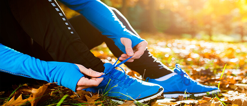 Woman Sitting in Fall Leaves Tying Her Shoe