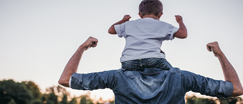 Son on Dad's Shoulder, both triumphant pose with biceps flexed, from behind, and outdoors