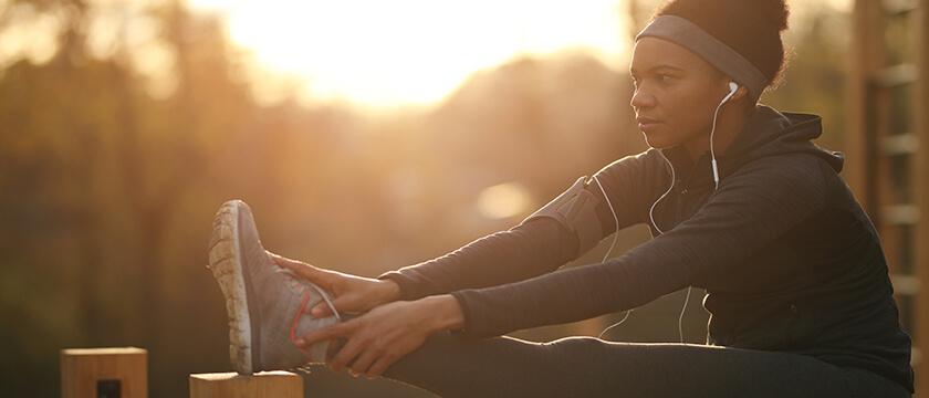 Runner Stretching with Her Leg Up on a Fence Post, focused and with Airbuds in.